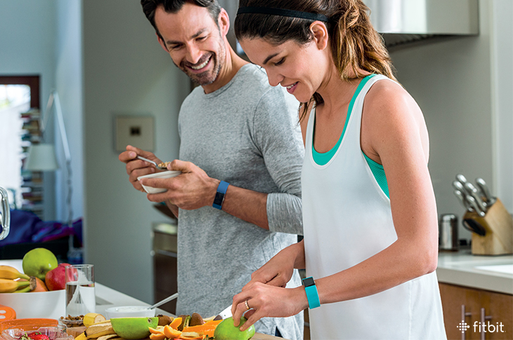Couple cooking healthy meal while wearing Fitbit trackers