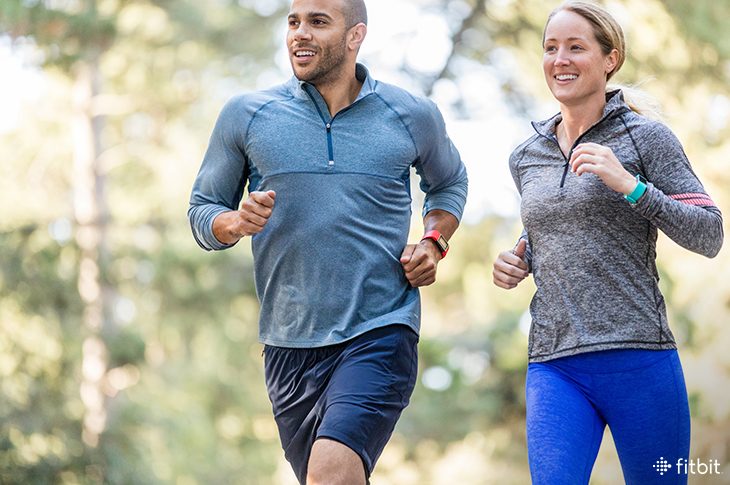 Man and woman running while wearing Fitbit trackers