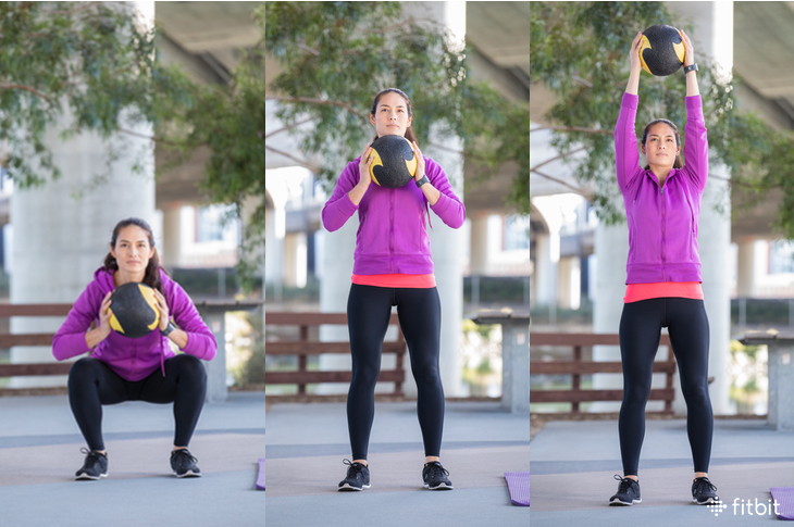 Woman performing a medicine ball squat-to-overhead.