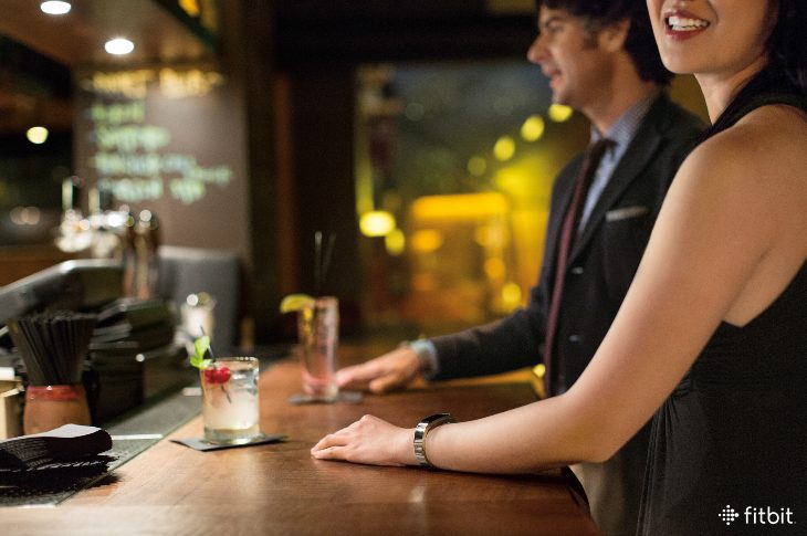 Woman drinking alcohol at a bar while wearing a Fitbit tracker