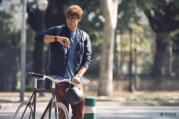 Man checks his Fitbit watch while pushing his bike.